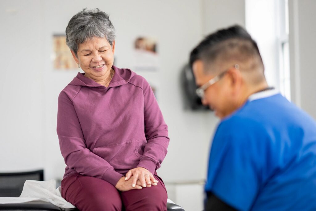 Smiling Senior Patient With Medical Professional During Routine Checkup In Bright Clinic Exam Room